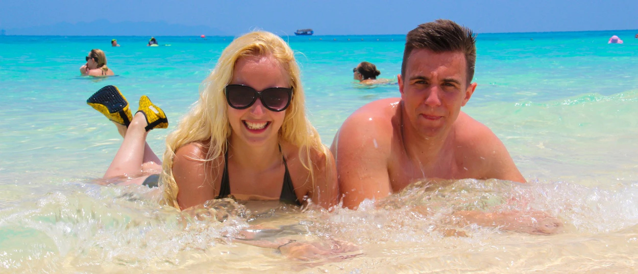 A smiling couple relaxes in the clear turquoise water on a sunny tropical beach in Phuket.