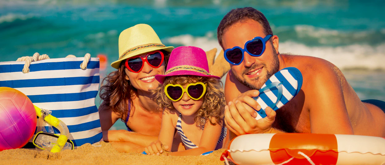 A happy family wearing hats and heart-shaped sunglasses relaxing on a sandy beach in Phuket.
