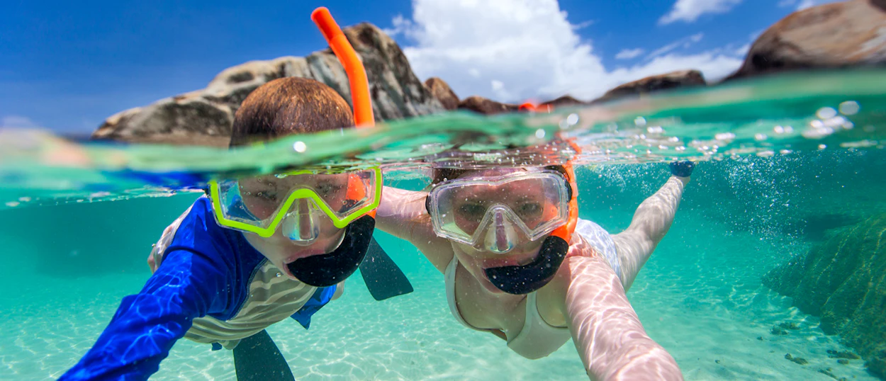 Happy snorkelers explore the clear turquoise waters near rocky islands under a sunny sky in Phuket.