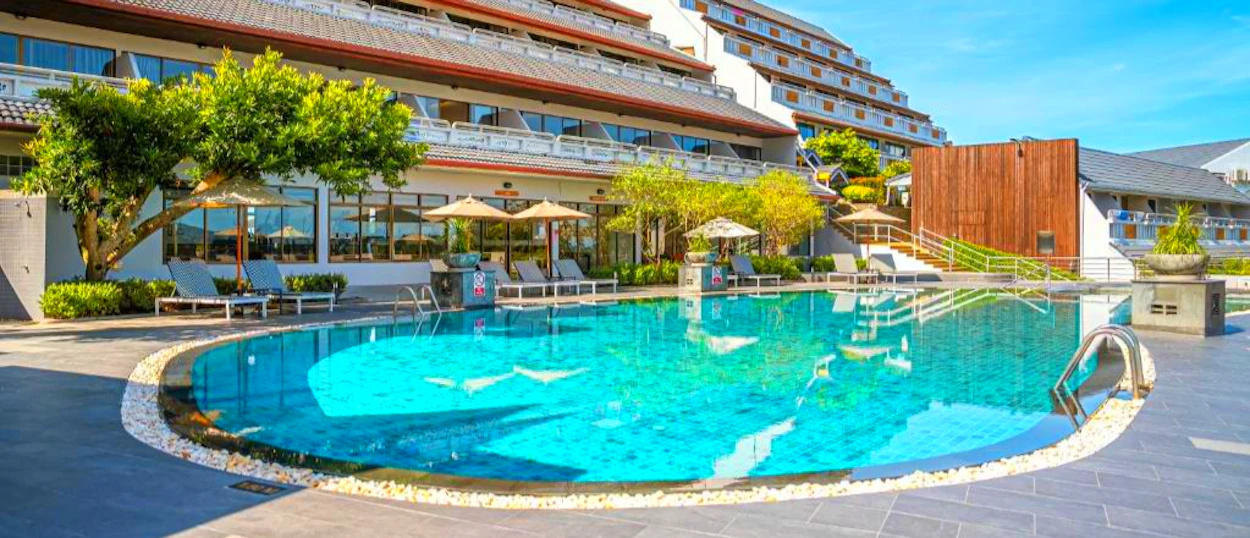 Relaxing hotel swimming pool with sun loungers and lush greenery under a blue sky in Phuket.