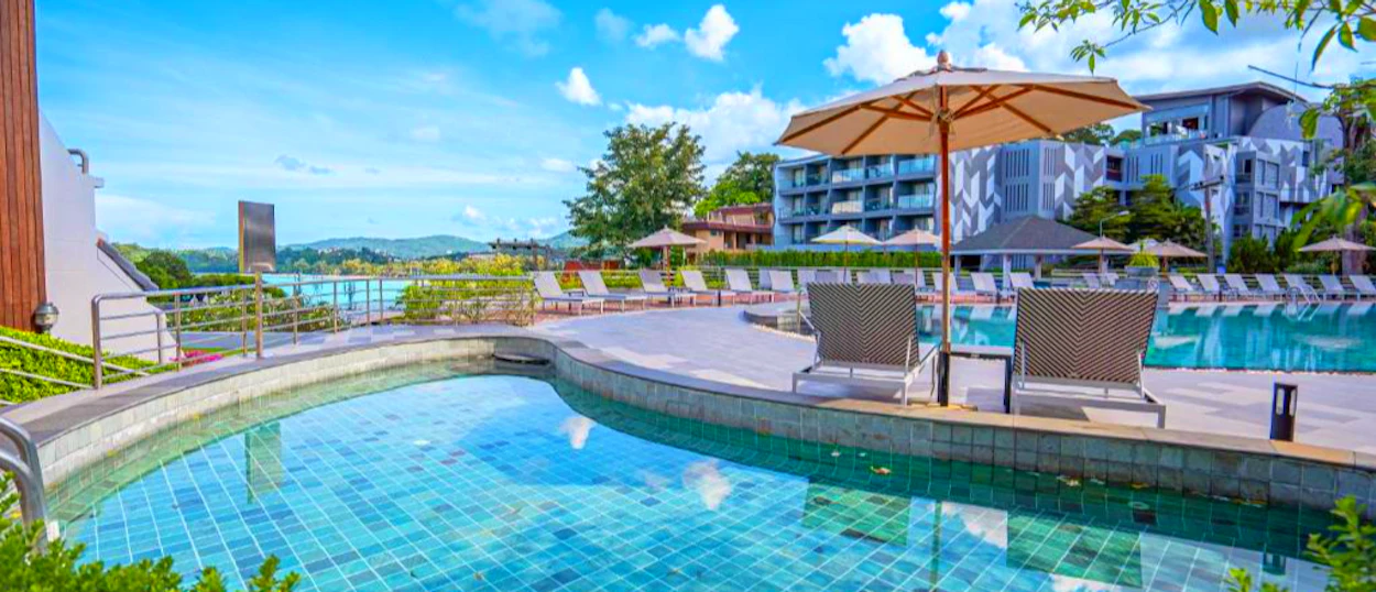 A beautiful resort pool area with sun loungers, umbrellas, and a view of the ocean in Phuket.