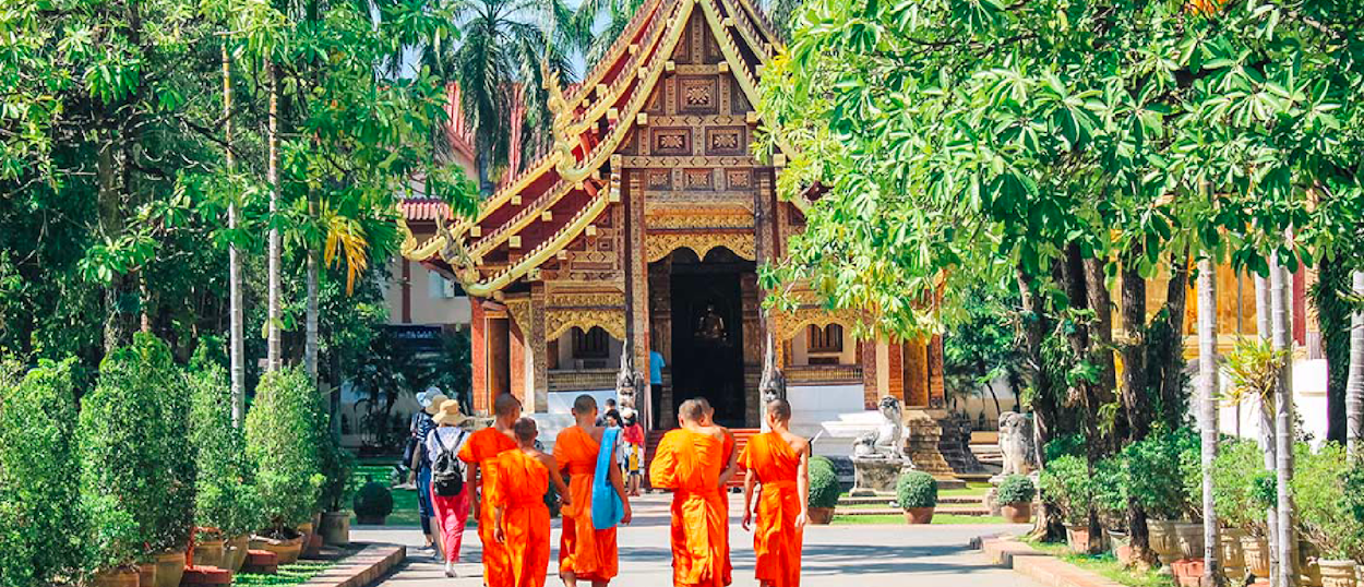 Monks in orange robes walking outside Chiang Mai temple during the backpacking tour