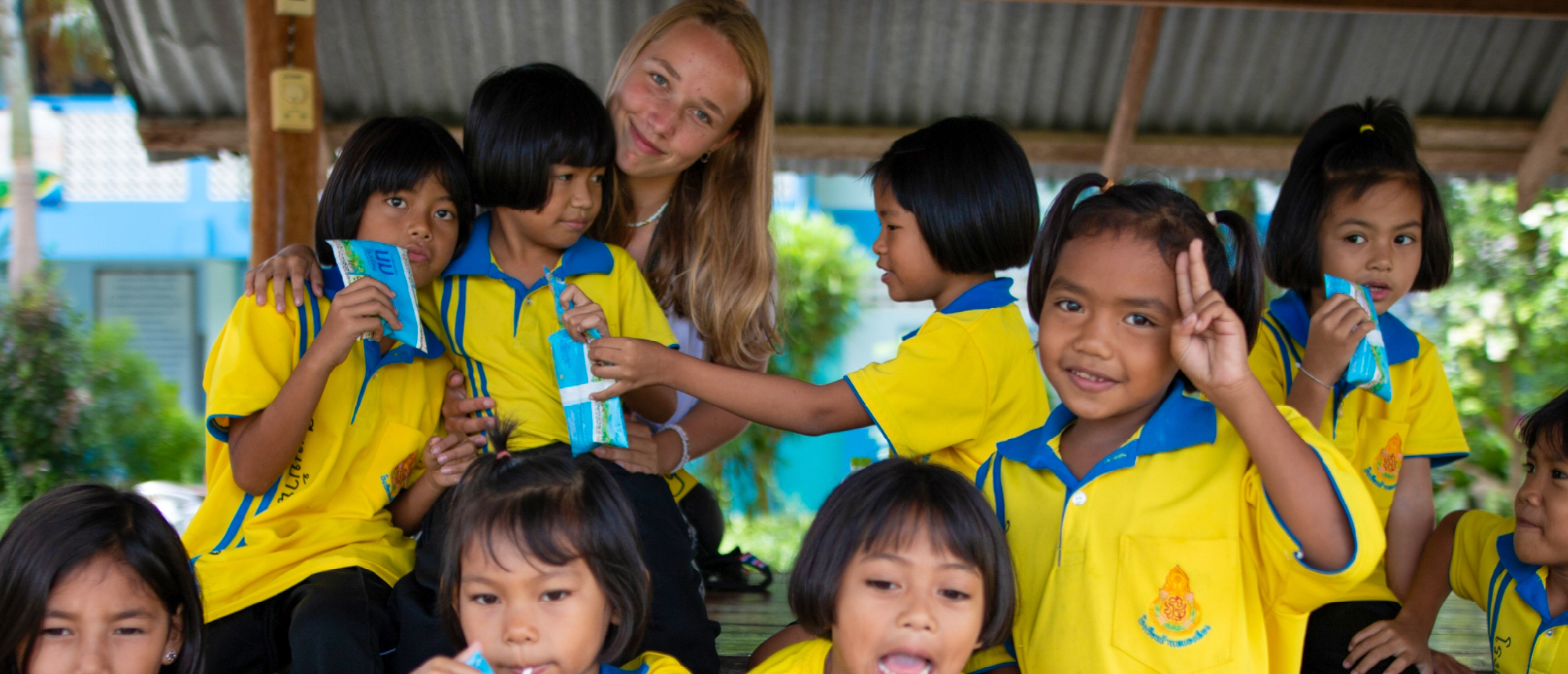 A smiling volunteer poses with cheerful Thai students in yellow uniforms during a school break.