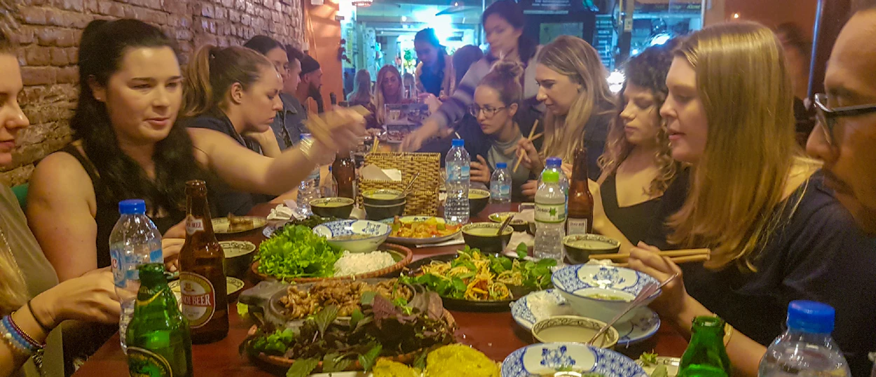 Travelers gather around a table laden with Vietnamese food, enjoying a communal dinner in Hanoi.