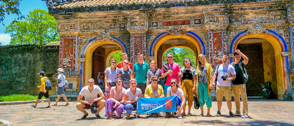 A group of happy backpackers posing in front of the ornate Imperial City gate in Hue, Vietnam.