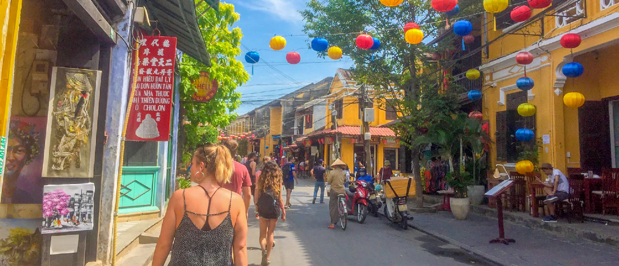Tourists stroll along a vibrant street in Hoi An, adorned with colorful lanterns and historic yellow buildings.
