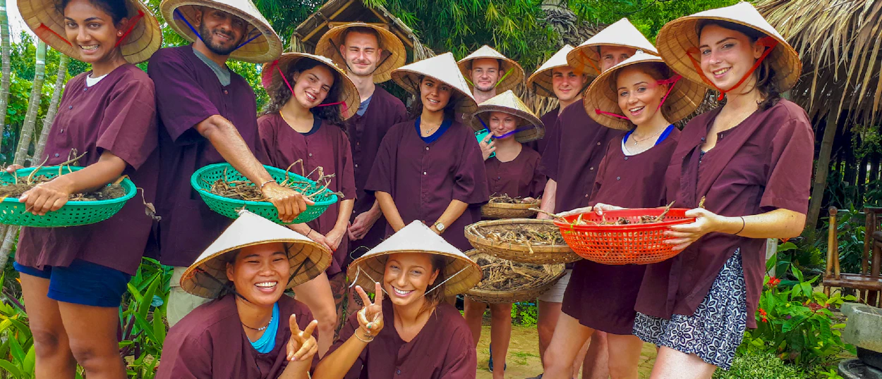A joyful group of travelers wearing conical hats and tunics at an organic farm in Hoi An.