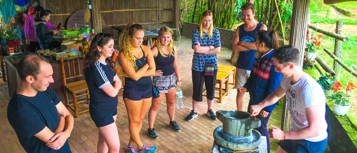 Travelers observe a local demonstrating traditional rice paper making with a grinding stone in Hoi An.
