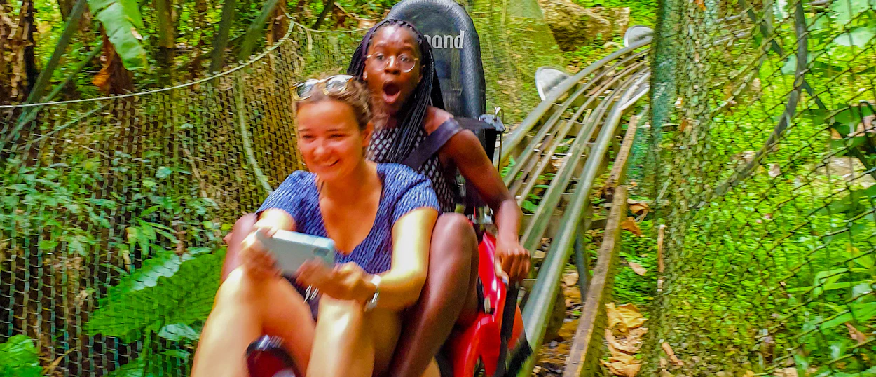 Two excited women ride an alpine coaster through lush green jungle in Dalat.