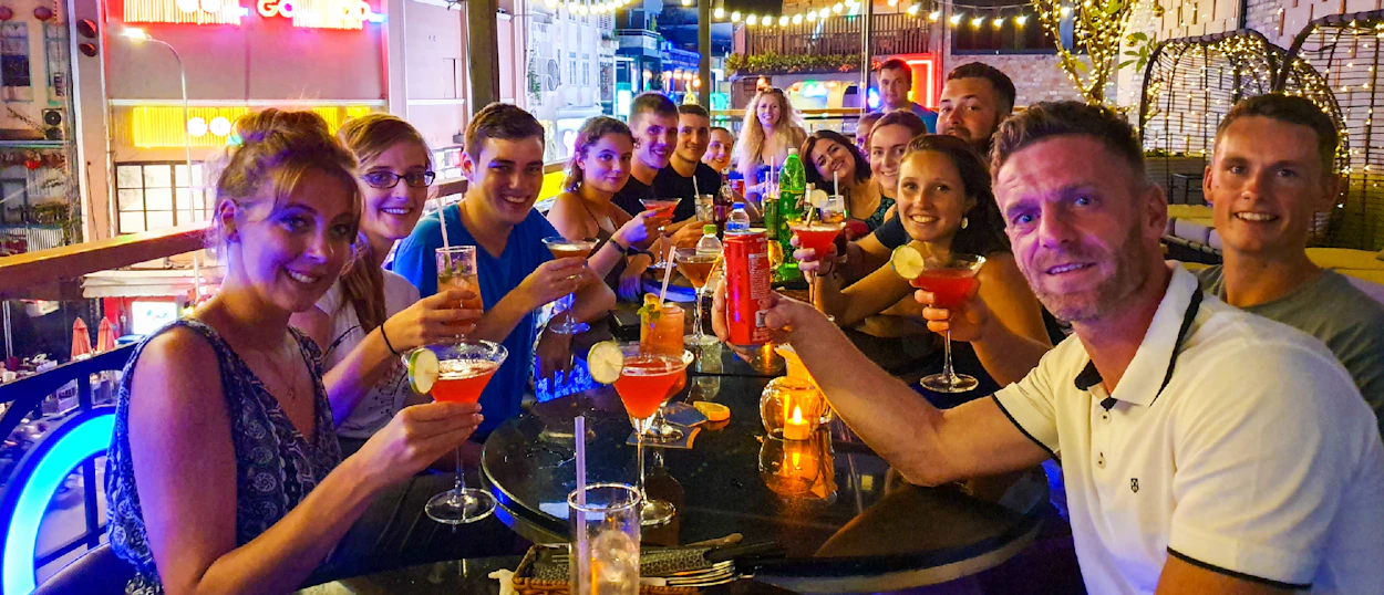 Happy travelers toasting with colorful cocktails at a vibrant, neon-lit bar in Saigon.