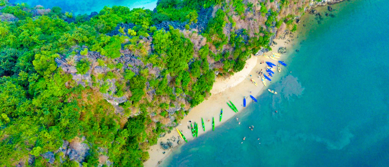 Aerial view of a sandy beach with many kayaks next to a lush green island in Vietnam.