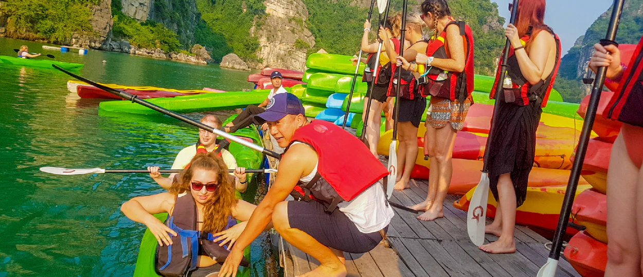 Adventurous travelers preparing to kayak on emerald water surrounded by majestic limestone karsts in Halong Bay.