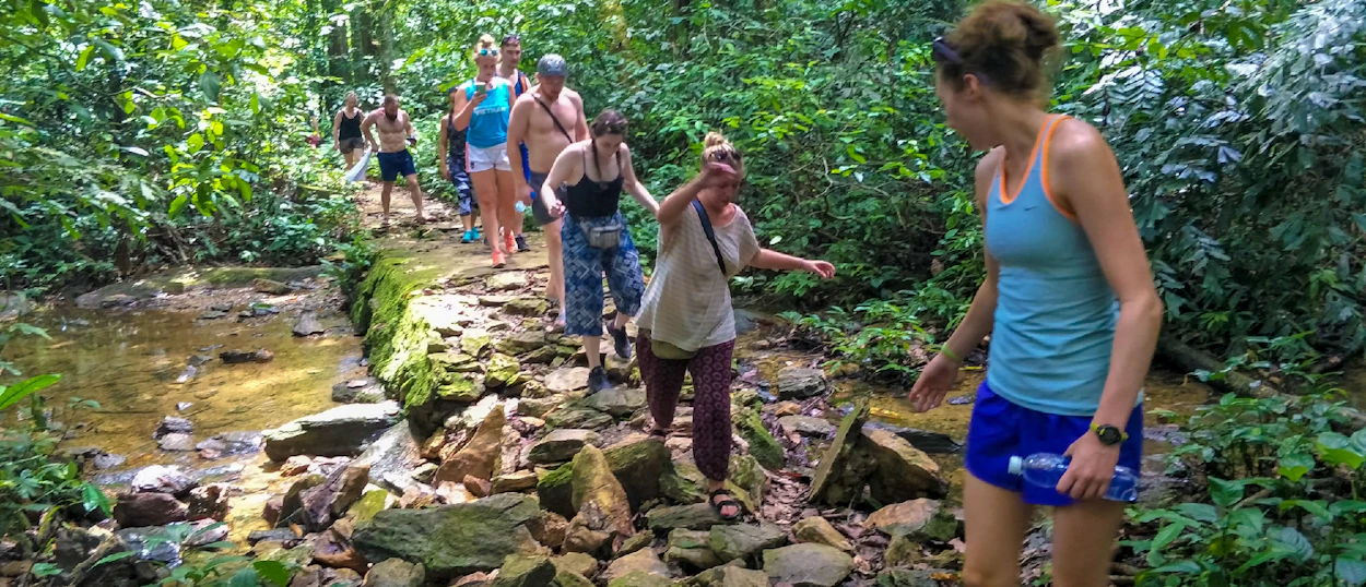 A group of backpackers carefully navigate a rocky jungle path next to a stream in Phong Nha.