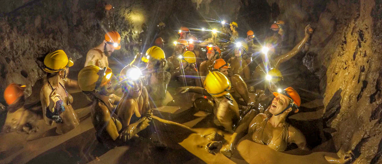 Adventurous travelers covered in mud, enjoying a natural mud bath inside a cave in Phong Nha.
