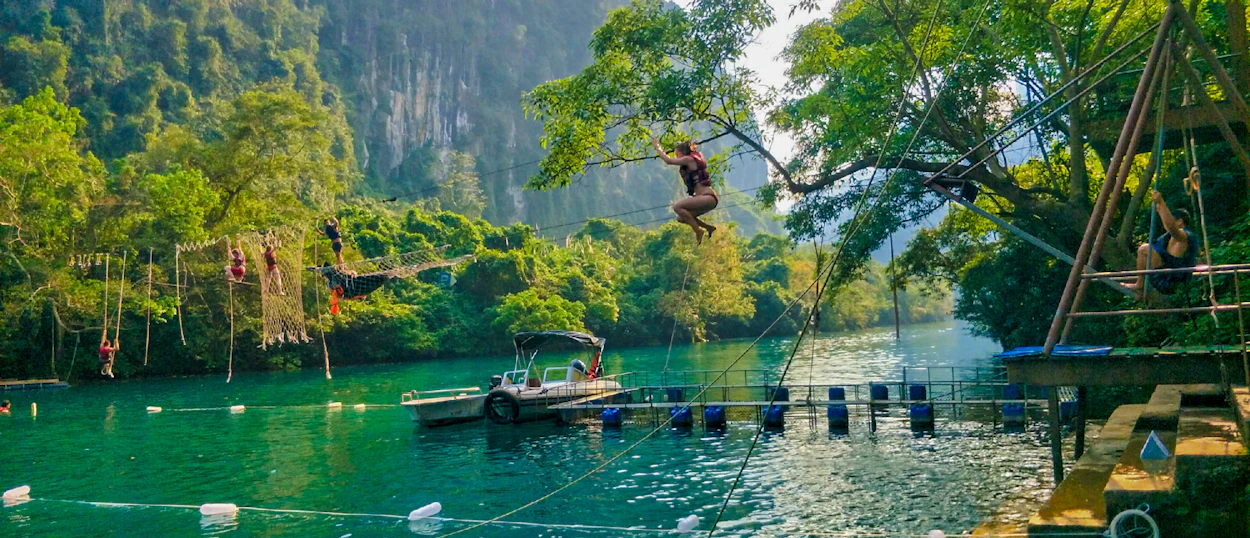 A person leaps from a tree swing into the vibrant turquoise river in Phong Nha, Vietnam.