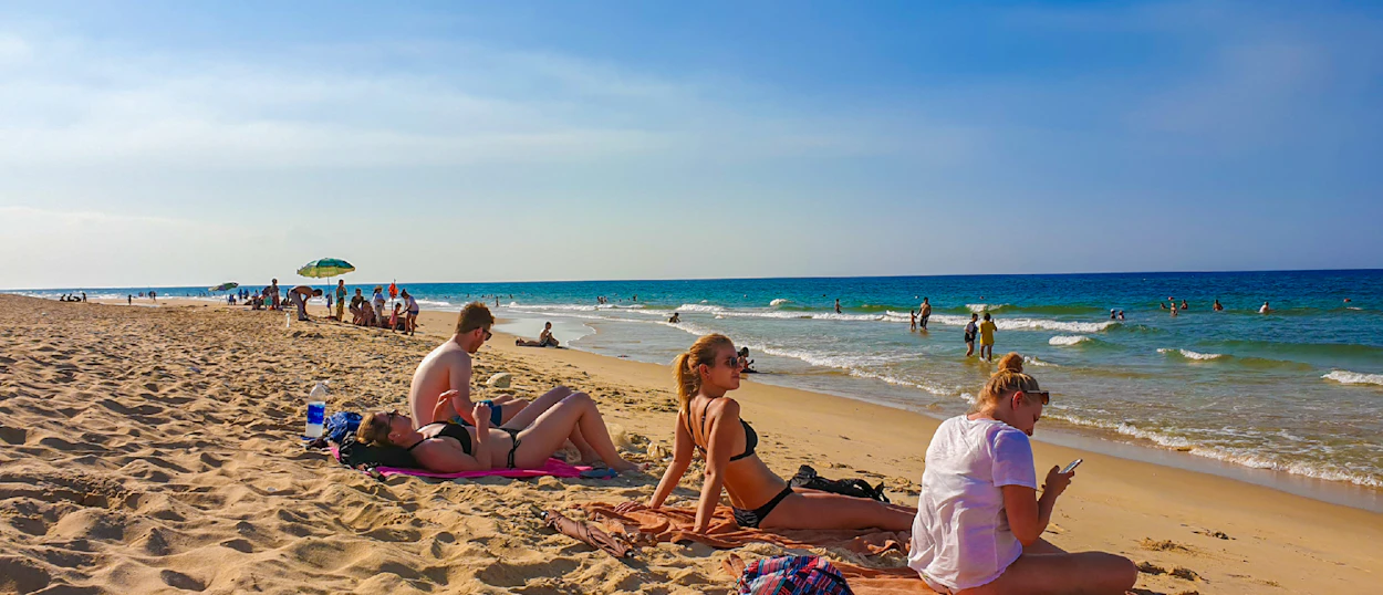Travelers relax and sunbathe on a wide sandy beach with blue ocean waters in Vietnam.