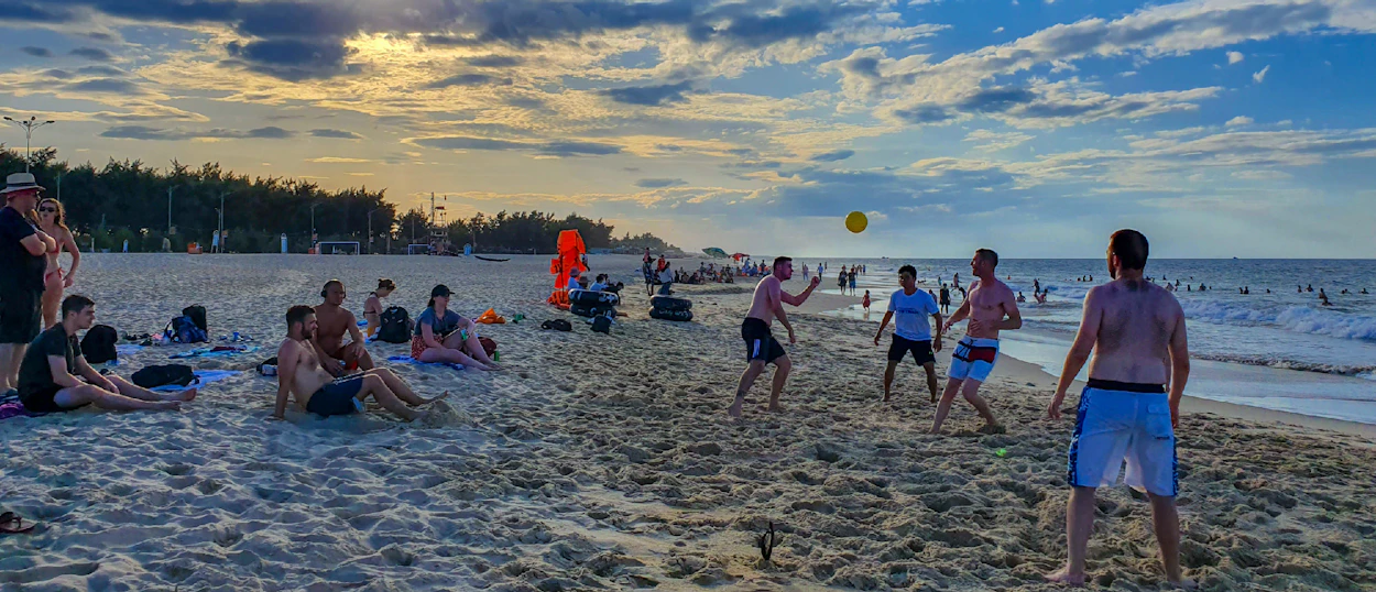 Friends play a ball game and relax on a wide sandy beach at sunset in Vietnam.