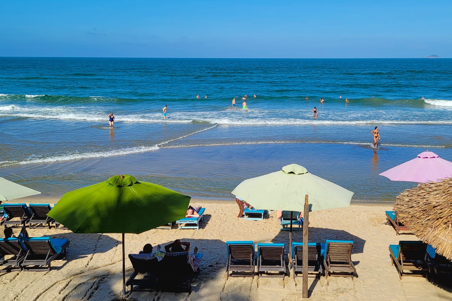 Sunny beach in Vietnam with people swimming in the ocean and relaxing under colorful umbrellas.
