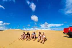 Five friends relax on golden sand dunes under a bright blue sky in Vietnam.