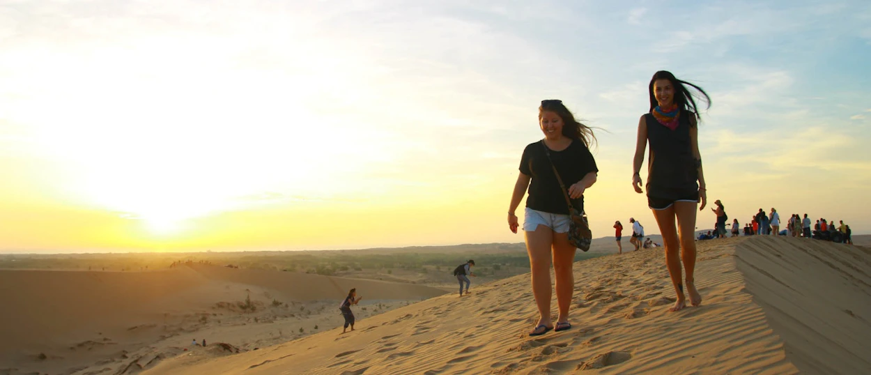 Two women walk down white sand dunes in Mui Ne during a beautiful sunrise.