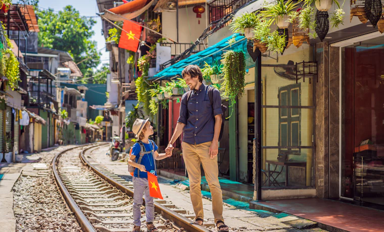 A father and son smile, holding hands on the railway tracks of a bustling Hanoi street.