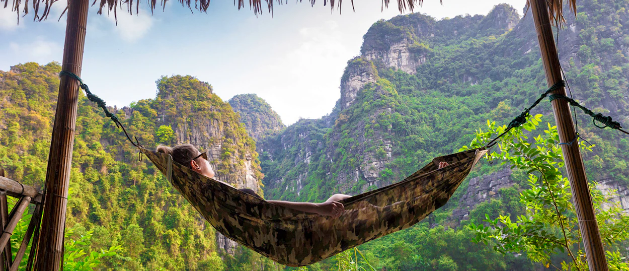 A person relaxes in a hammock overlooking the stunning limestone karsts of Ninh Binh, Vietnam.