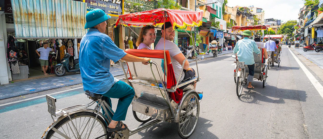 Two travelers experience a traditional cyclo ride through the lively Old Quarter of Hanoi.