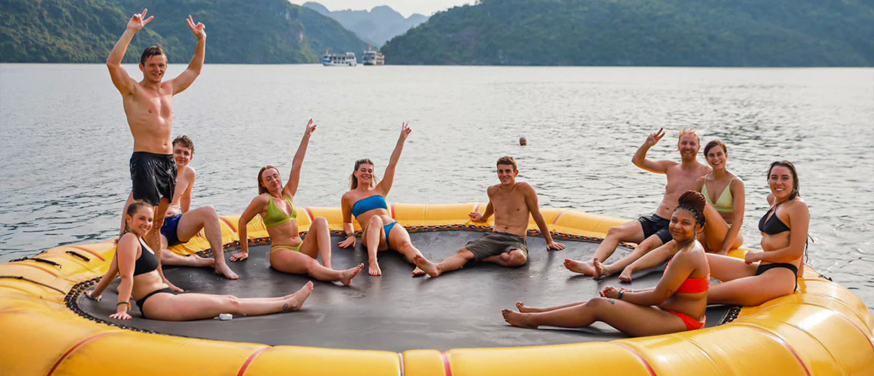 Happy backpackers wave from a large yellow inflatable trampoline in Vietnam's scenic Ha Long Bay.