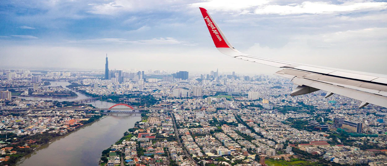 An airplane wing overlooks the sprawling Ho Chi Minh City with its river, bridges, and tall skyscrapers.
