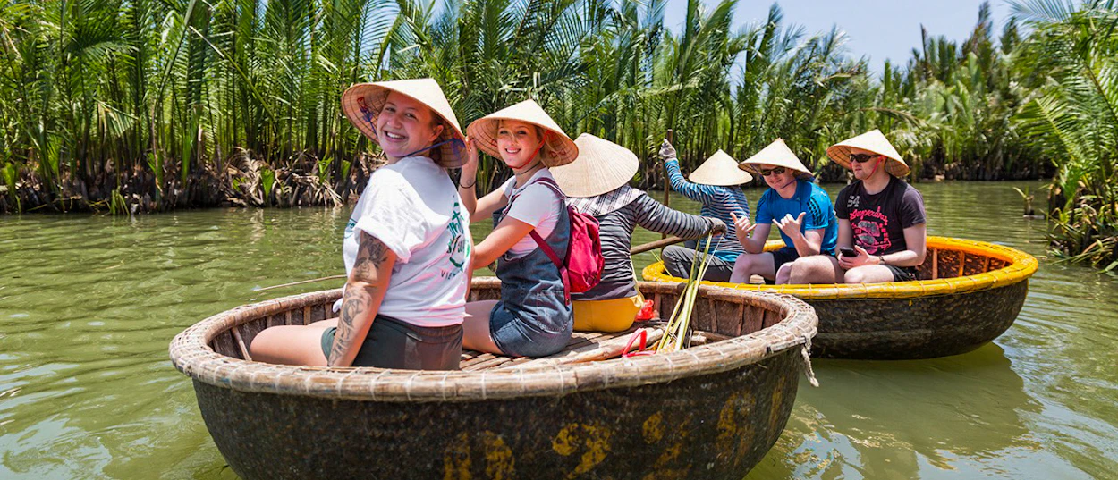 Tourists in conical hats enjoy a basket boat ride through a lush coconut grove in Hoi An.