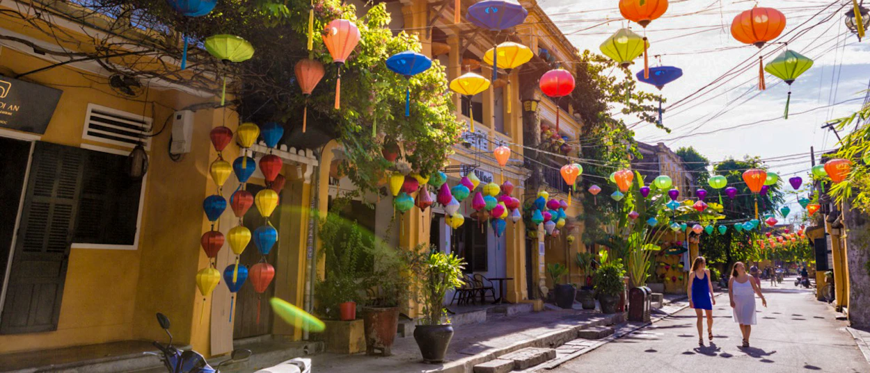 Two women walk along a vibrant street in Hoi An, adorned with many colorful lanterns.