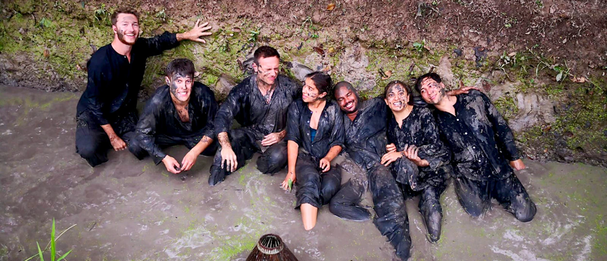 Happy travelers covered in mud, sitting in a muddy stream during a fun Mekong Delta experience.