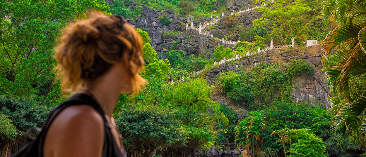 A woman gazes at the winding steps of Dragon Mountain, Ninh Binh, surrounded by lush green karst landscape.