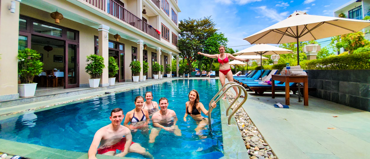 Six happy travelers enjoy a refreshing swim in a sunny hotel pool in Hoi An, Vietnam.