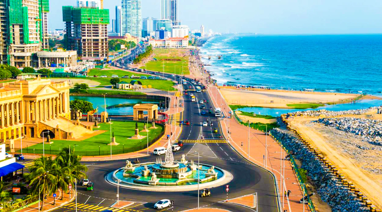 A bustling coastal city in Colombo, Sri Lanka, with a busy road, modern buildings, and a wide beach.