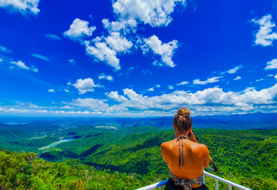 Woman from behind admires the expansive green landscape and blue sky from a viewpoint in Vietnam.